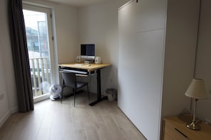 Ein kleines, modernes Zimmer mit Schreibtisch, Stuhl, Computer und Standventilator.