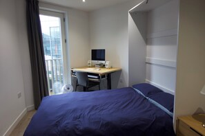 Ein Schlafzimmer mit einem Bett, einem Schreibtisch mit Computer und einem Fenster.