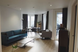 Ein modernes Wohnzimmer mit Sofa, Couchtisch und Sesseln. Es gibt einen Essbereich mit Tisch und Stühlen sowie einen Balkon mit Blick.
