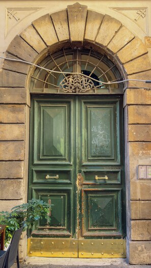 A green double door with a decorative metal arch above it, set in a stone wall. - Charming Apartment on the Rome Terrace Near the Pantheon (Roma)