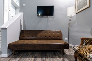 A room with a brown leather sofa, a television mounted on the wall, a floor lamp, and a patterned armchair. - Charming Apartment on the Rome Terrace Near the Pantheon (Roma)