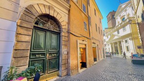 A cobblestone street with a historic building featuring a large green door and an arched window. - Charming Apartment on the Rome Terrace Near the Pantheon (Roma)