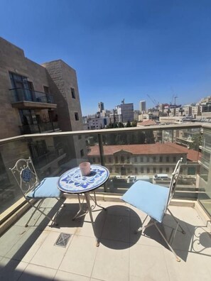 A rooftop terrace with a table and chairs, a clear view of the cityscape, and a glass railing. - Mounbaz Royal Suites (Jerusalem)