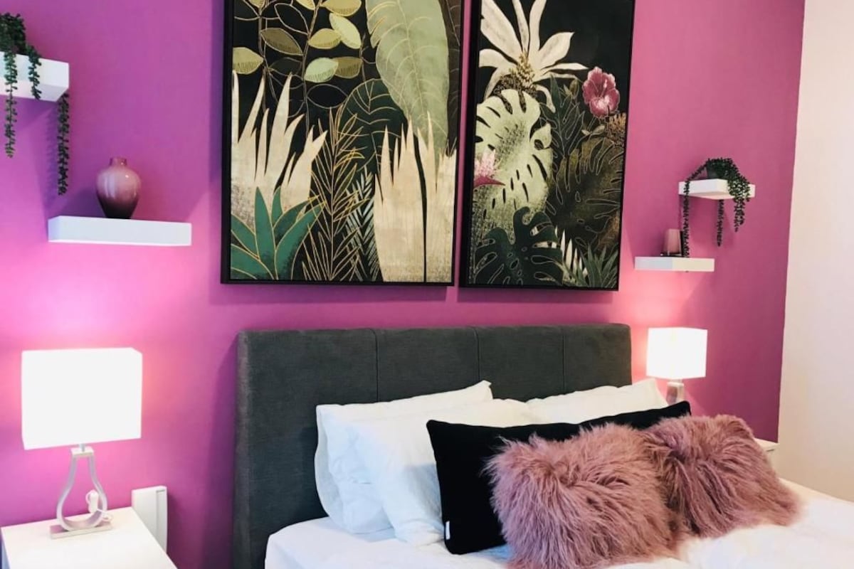 A bedroom with a bed, white bedding, a dark headboard, and two wall-mounted artworks depicting foliage.