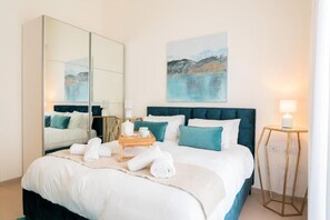 A hotel room with a bed, a large mirror, a painting on the wall, and a bedside table with a lamp. - Mounbaz Royal Suites (Jerusalem)