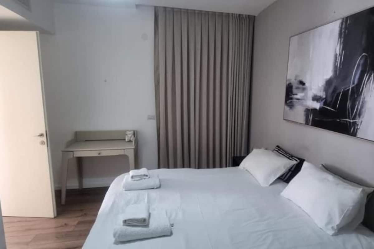 A hotel room with a bed, a desk, a chair, and a painting on the wall.