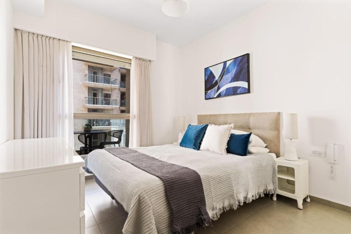 A hotel room with a bed, bedside table, and a window with curtains.