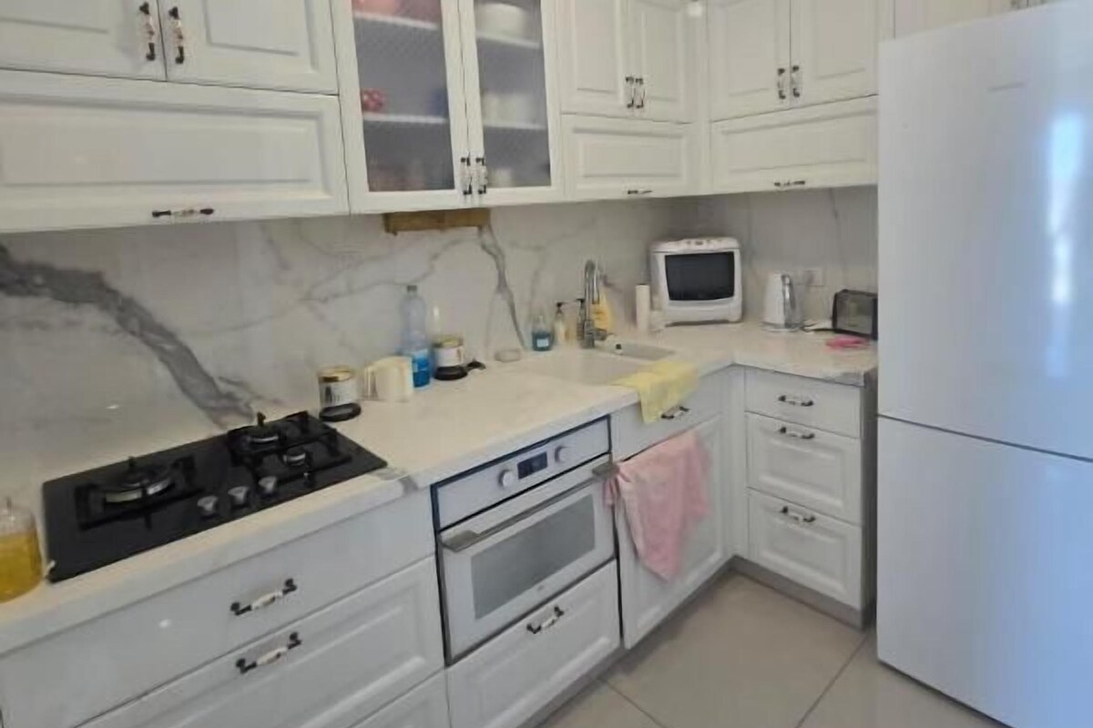 A kitchen with white cabinets, a stove, oven, microwave, and a refrigerator.