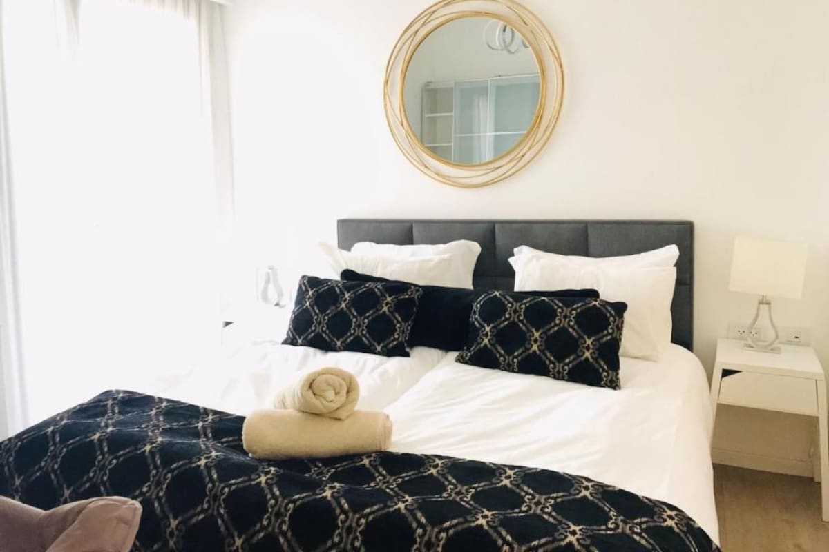 A hotel room with a bed, a bedside table, a lamp, and a mirror on the wall.