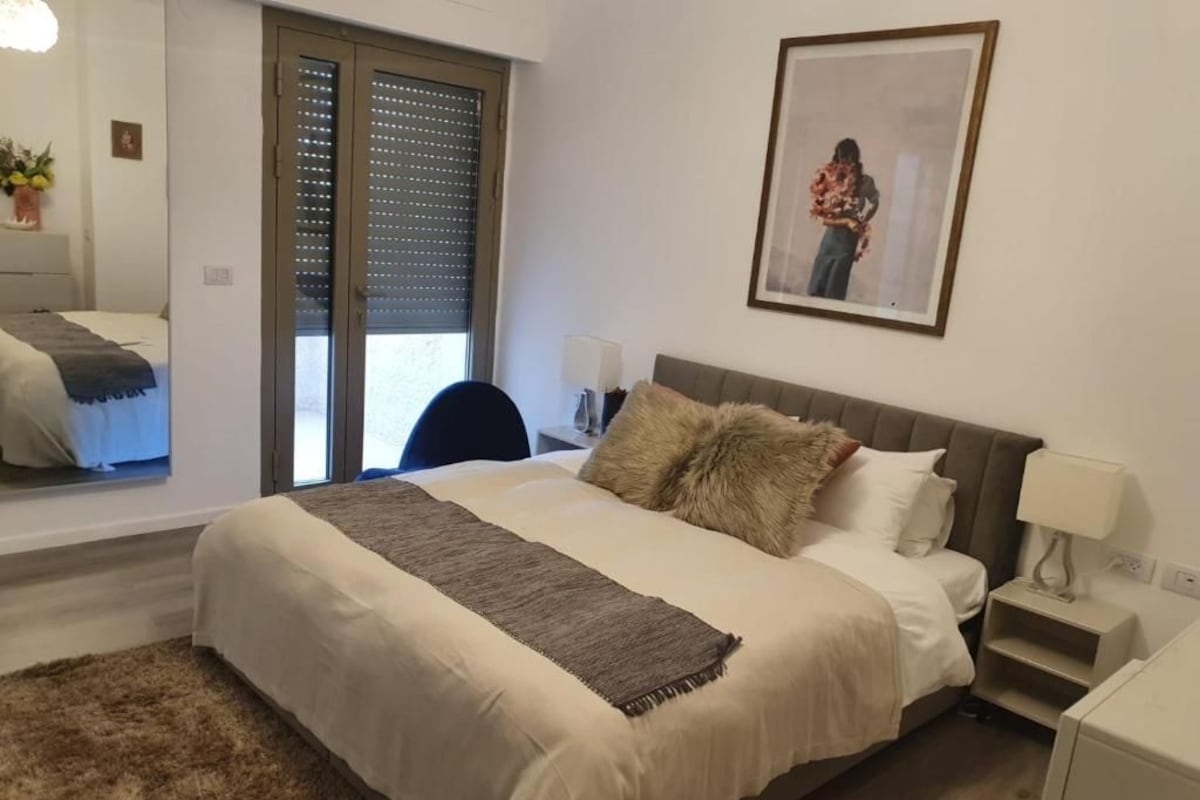 A bedroom with a bed, bedside tables, a lamp, a picture on the wall, and a window with blinds.
