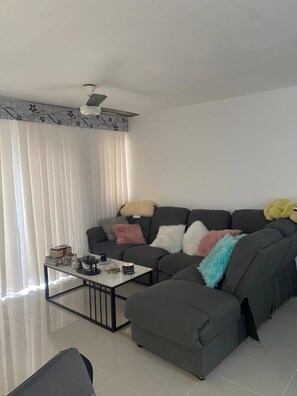 Ein modernes Wohnzimmer mit einer Eckcouch, einem Glastisch und einem Deckenventilator.