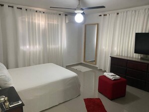 Une chambre d’hôtel avec un lit, une télévision, un pouf rouge, un miroir et un ventilateur de plafond.