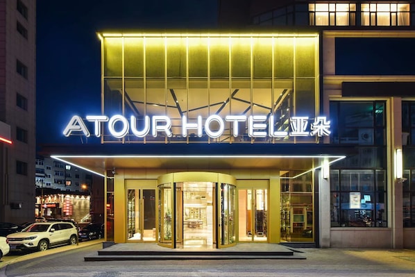 A hotel entrance with a glass facade, a neon sign, and a modern design.