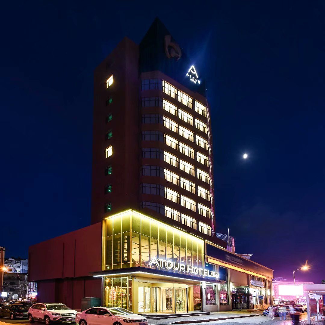 Een meerlaags hotel met een opvallend ATOUR HOTEL bord, een zichtbaar logo en een goed verlichte gevel.