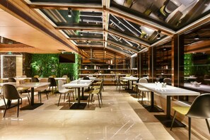 Un restaurante moderno con techo alto, varias mesas de comedor y una pared verde.