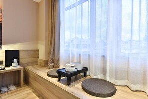 A modern hotel room with a wooden floor, a small black table with a tray, a cushioned bench, and a window with sheer curtains. - Atour Hotel  Lvshunkou centralsquare (Dalian)