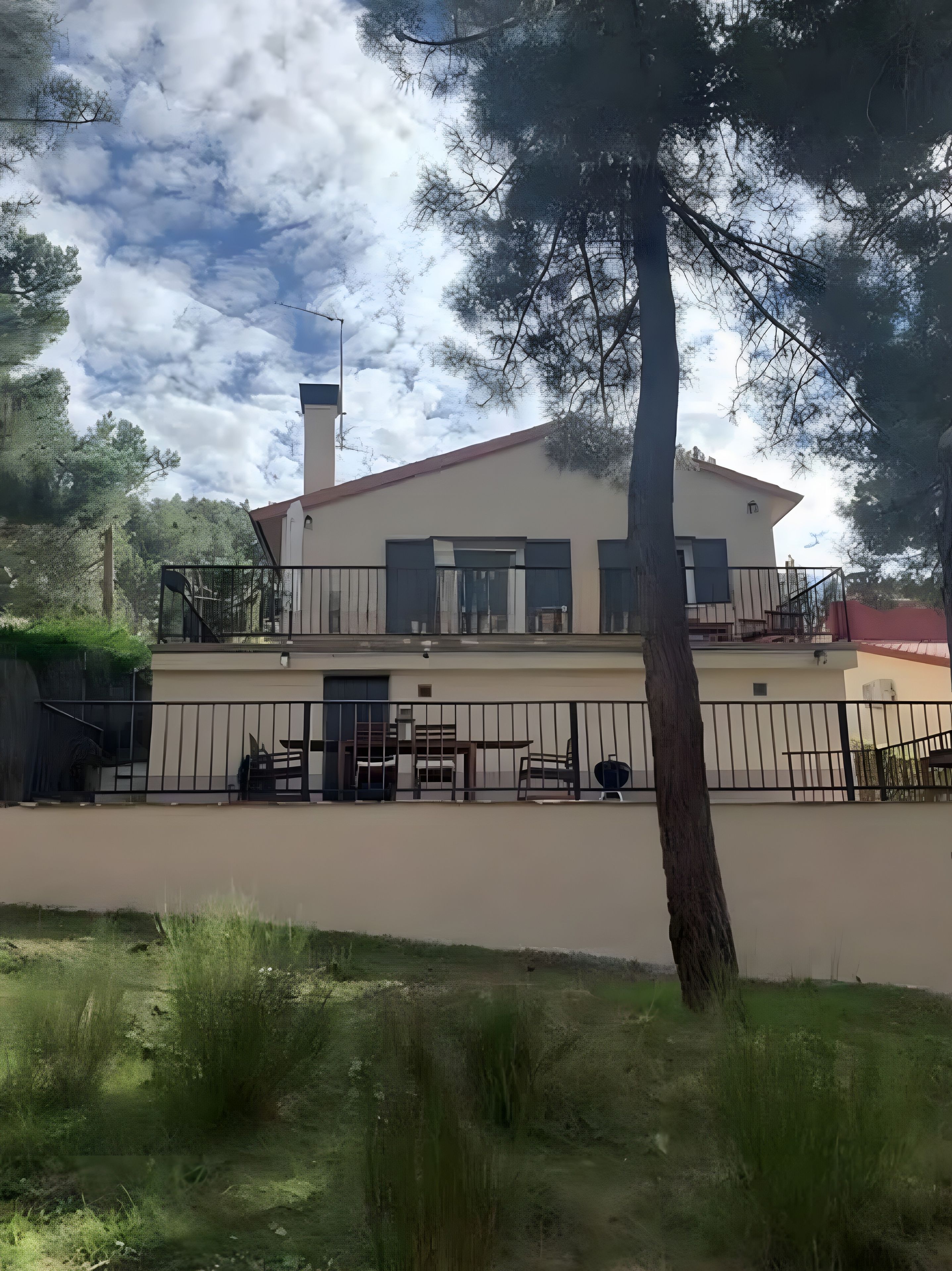 A two-story building with a balcony, a fenced outdoor area, and a view of the sky.