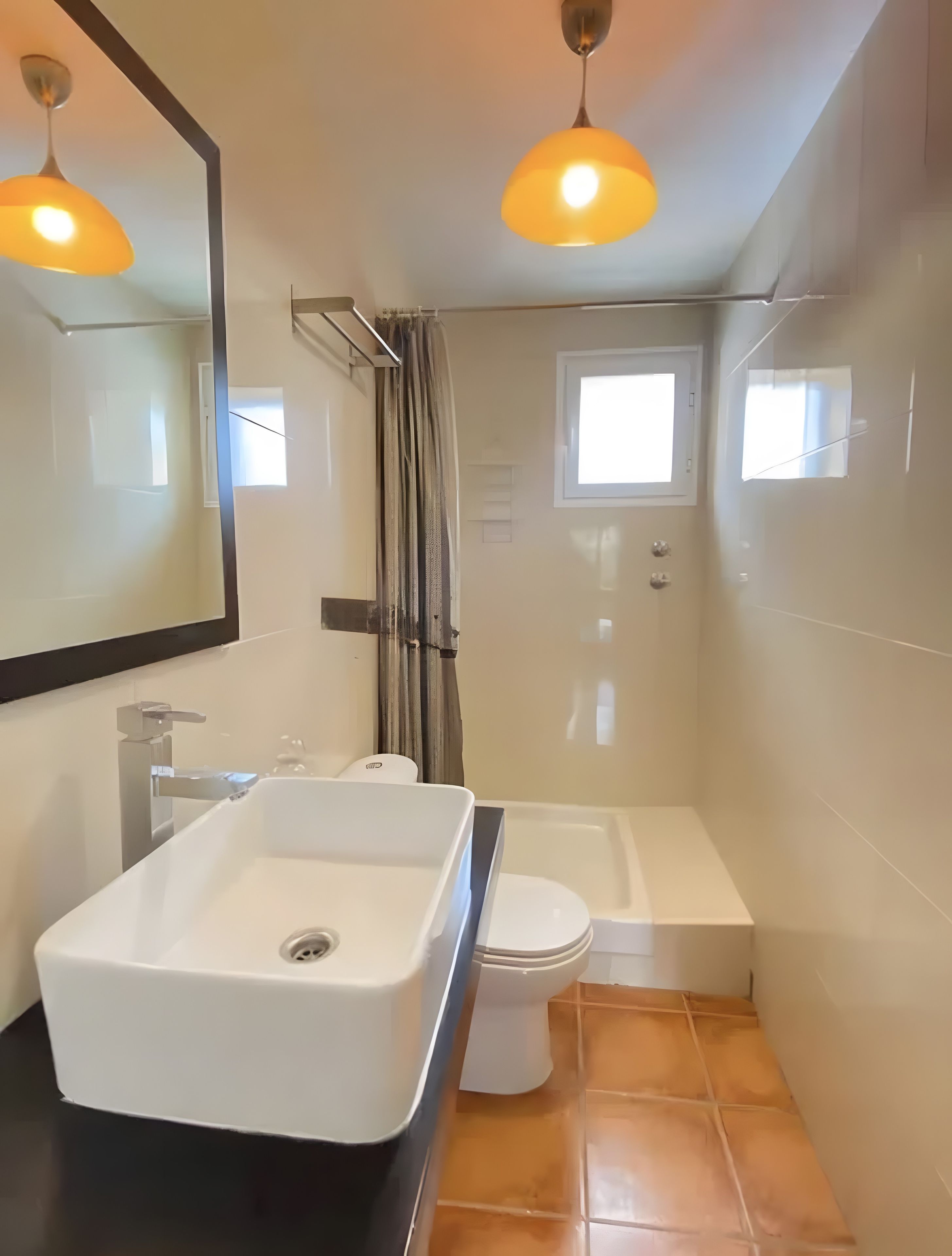 A modern bathroom with a white sink, a toilet, and a bathtub. There are two pendant lights and a window.