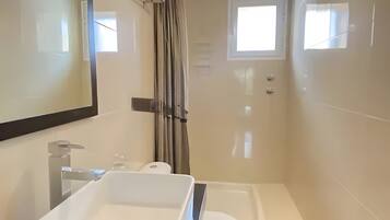 A modern bathroom with a white sink, a toilet, and a bathtub. There are two pendant lights and a window.