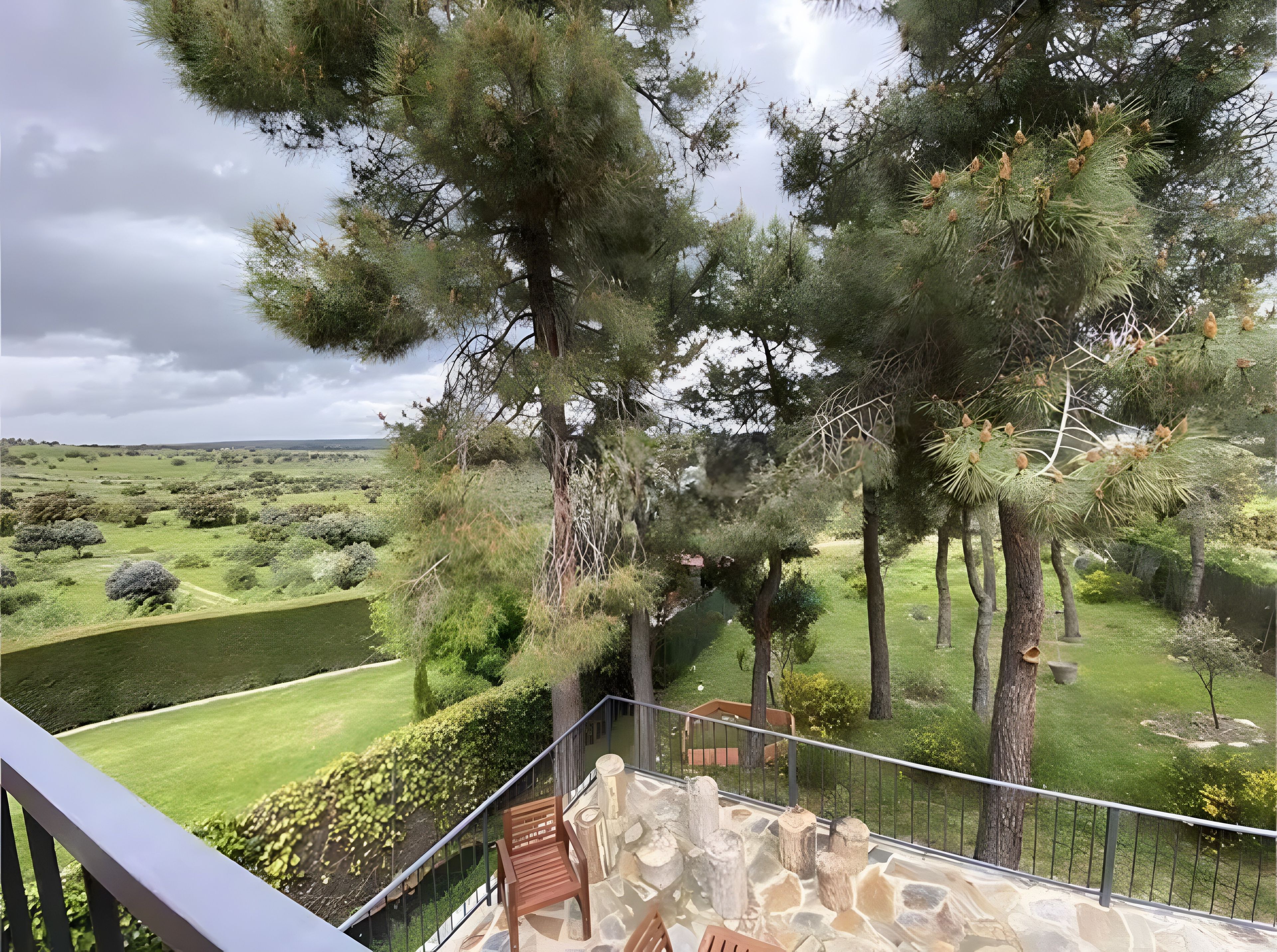 Un balcón con piso de piedra, con vistas a un jardín bien cuidado con diversos árboles y arbustos.