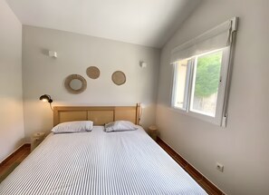 A bedroom with a bed, bedside lamps, a window, and wall decor.