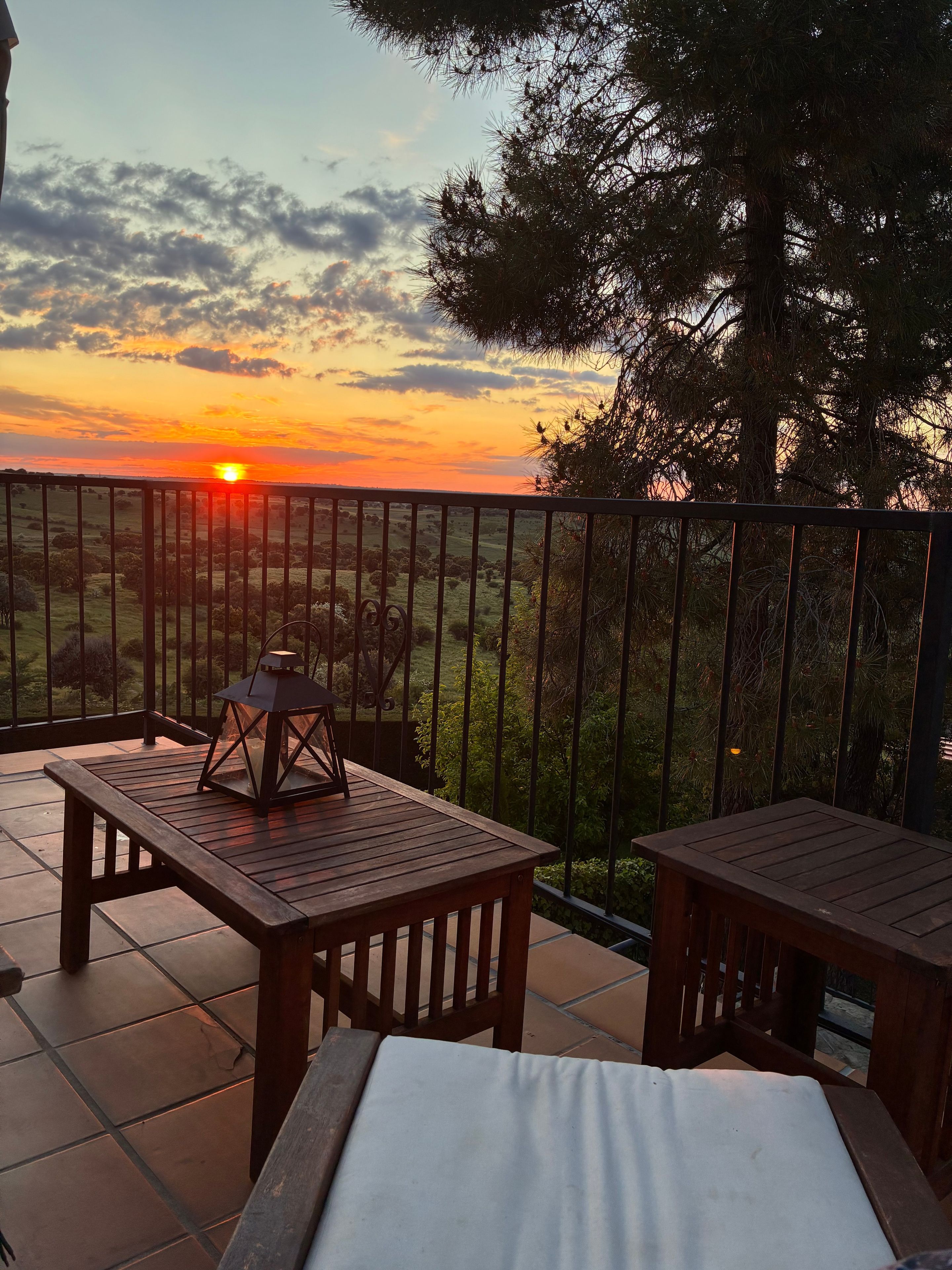 Eine Terrasse mit Blick auf den Sonnenuntergang, einem Holztisch und einer Laterne.