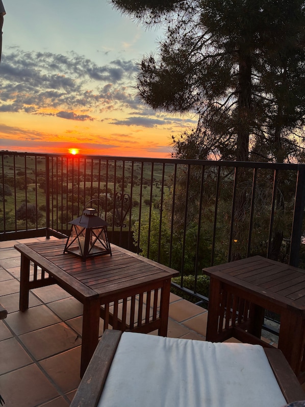A terrace with a view of the sunset, a wooden table, and a lantern.