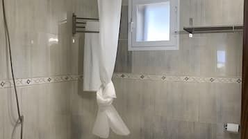 Un baño con bañera, ducha, inodoro y ventana con lámpara.