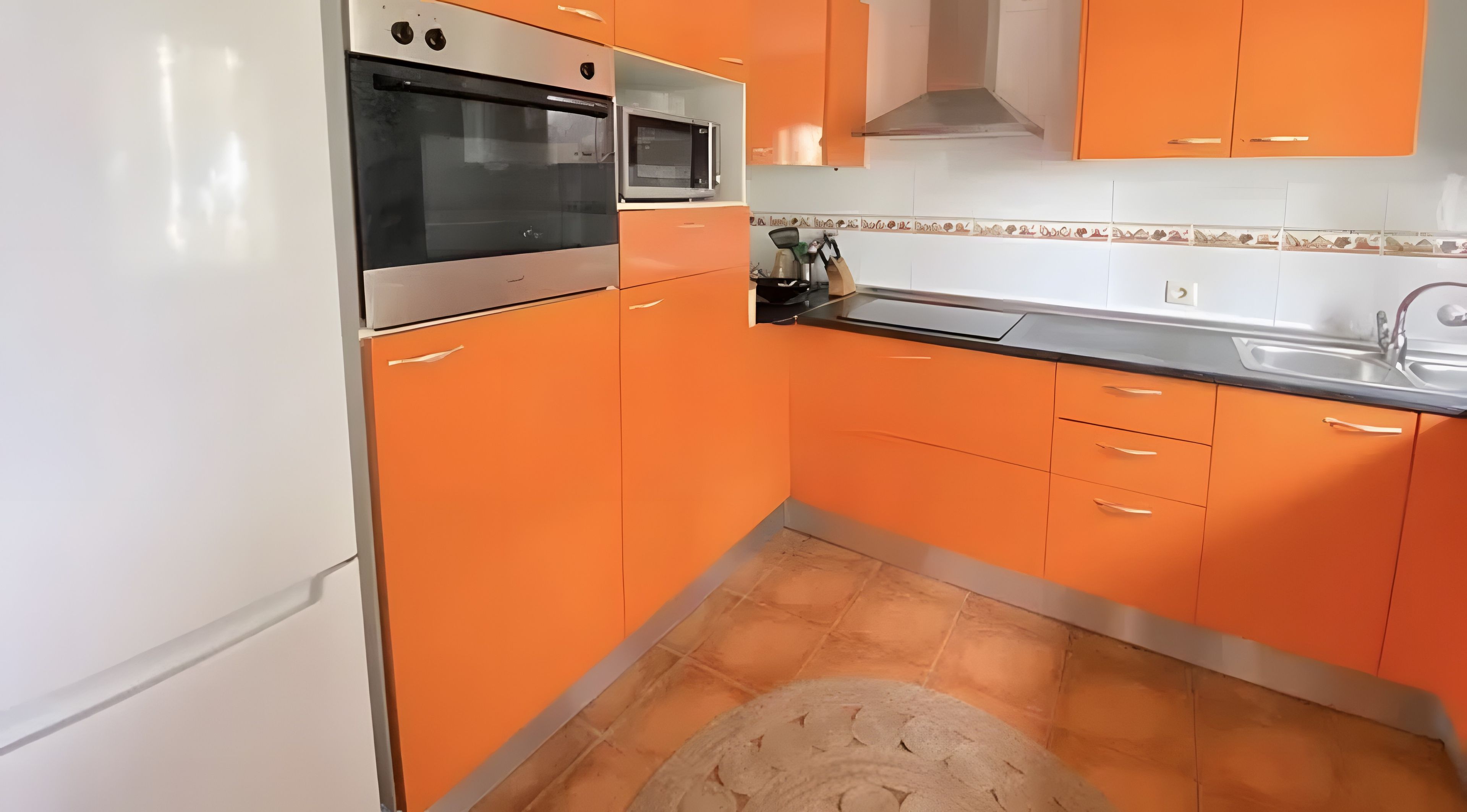 Una cocina con armarios color naranja, un microondas y un horno de acero inoxidable.