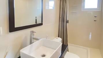 Un baño con lavamanos blanco, espejo, inodoro y ducha.