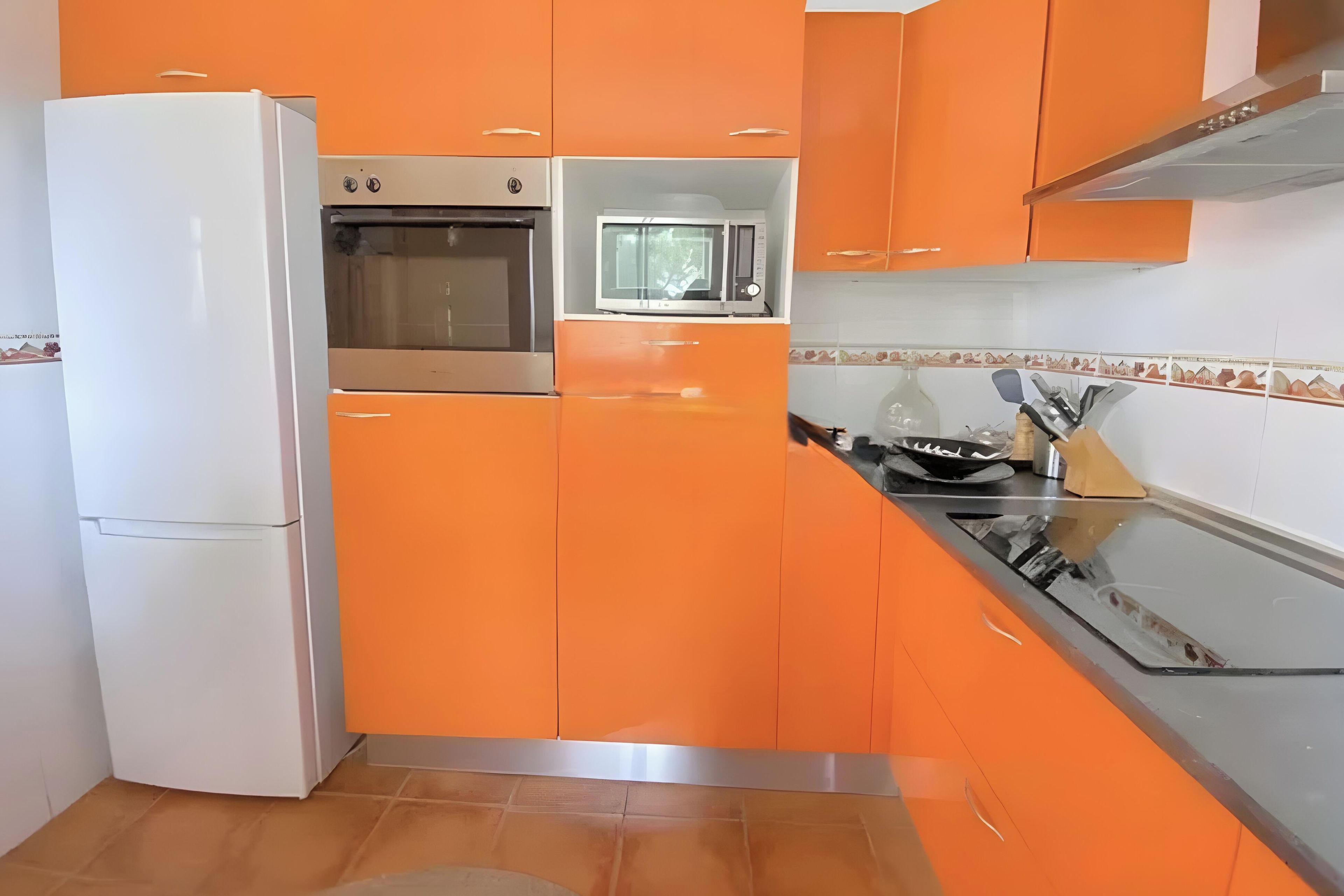 Una cocina con gabinetes naranja, un refrigerador blanco y una estufa.