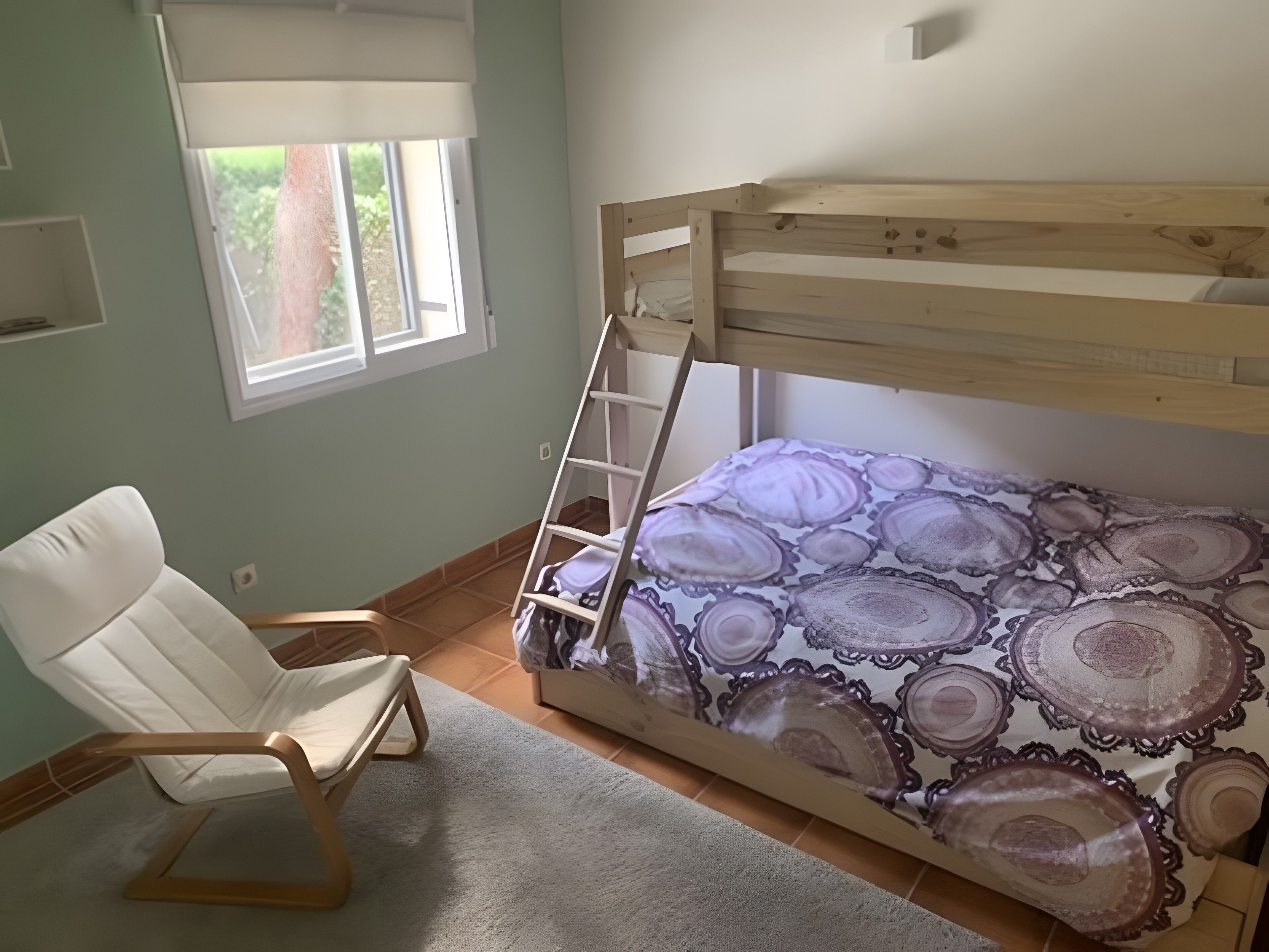 Une chambre avec un lit superposé, une chaise, une fenêtre et une couvre-lit à motifs.
