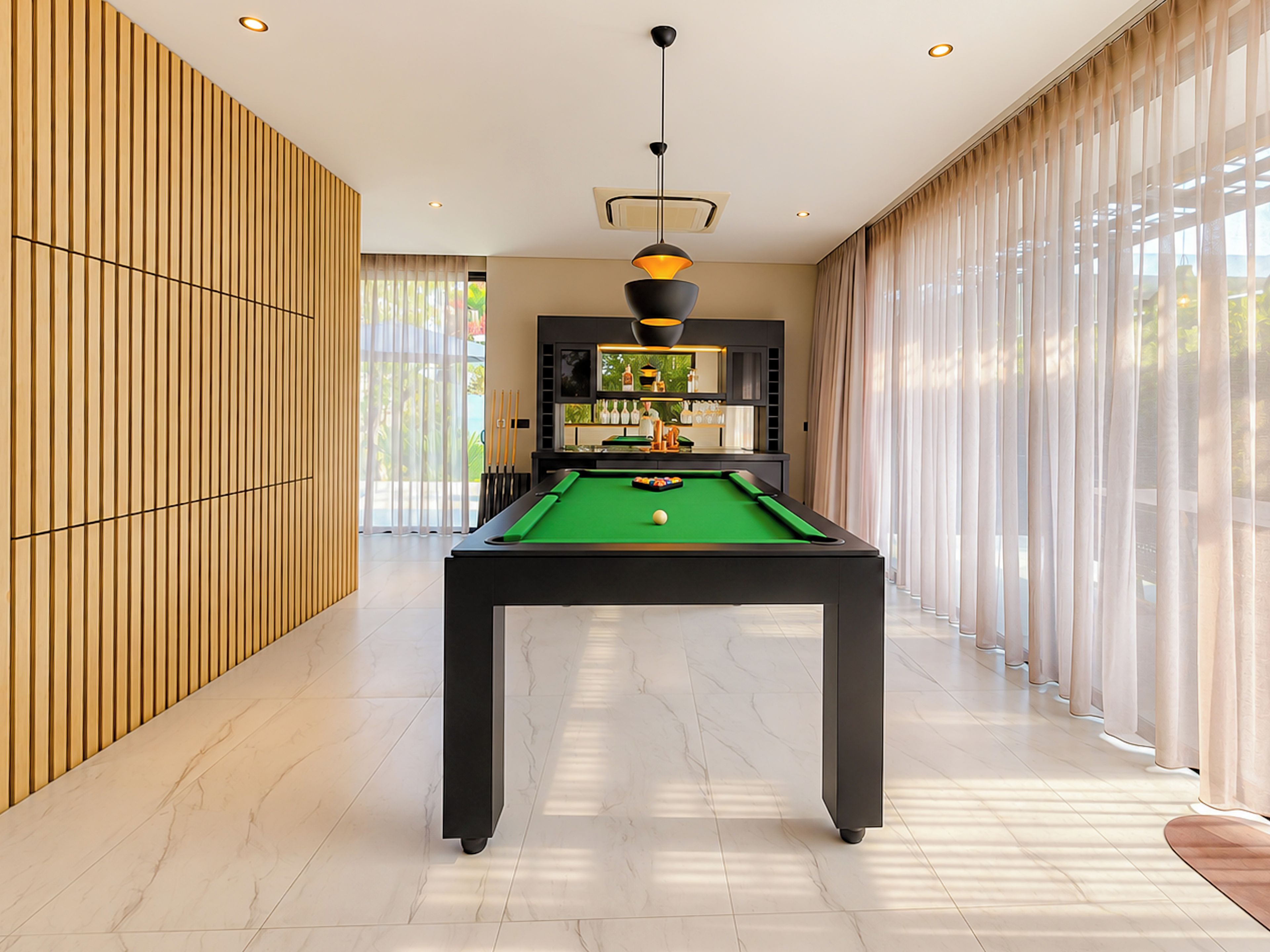 Una mesa de billar en una habitación bien iluminada con diseño moderno, ventanas amplias y vistas a zonas verdes al exterior.
