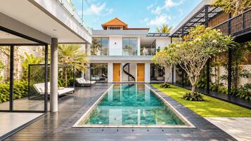 A modern house with a swimming pool, outdoor seating, and a staircase leading to the upper floor.