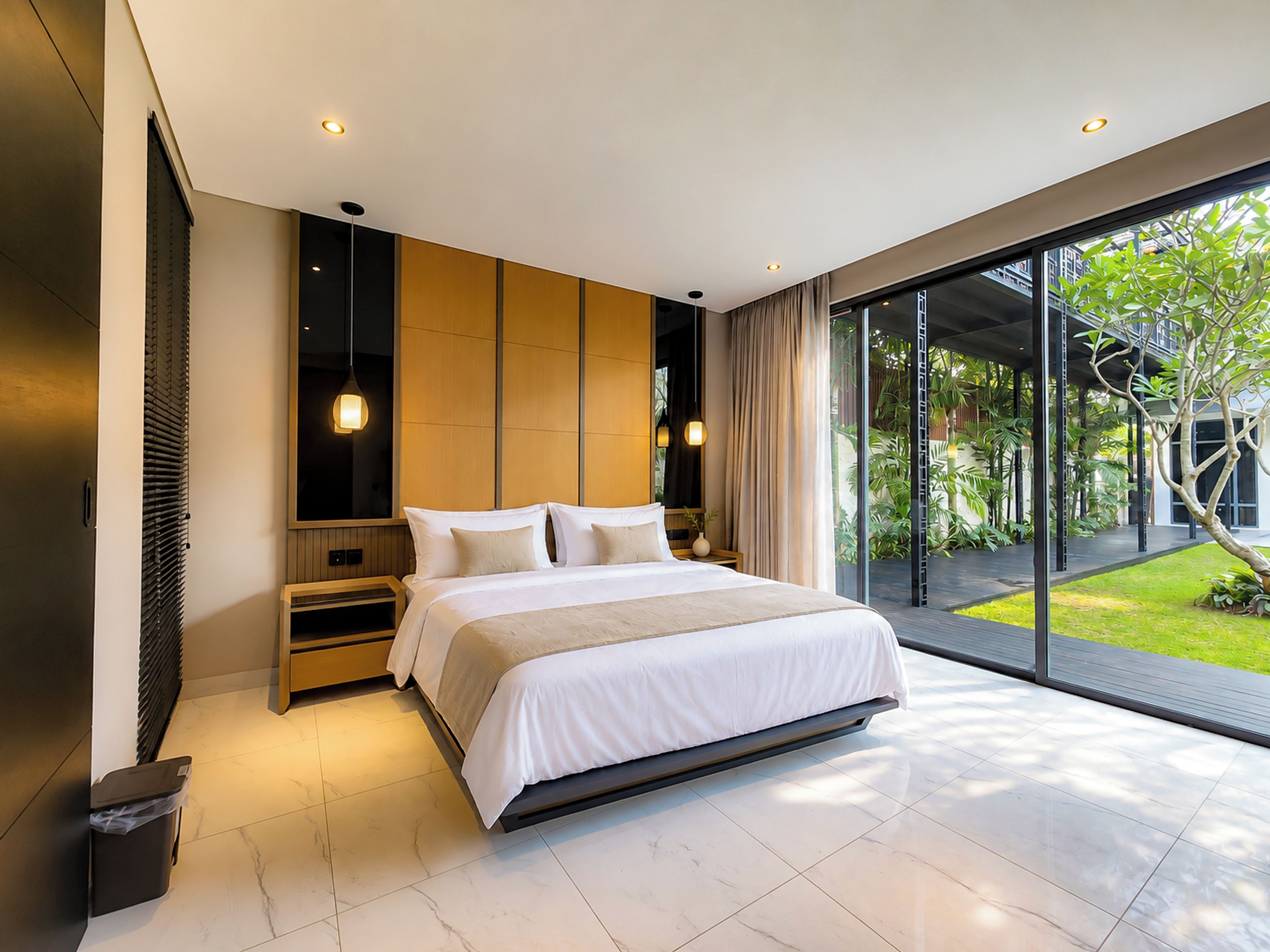 A modern bedroom with a large bed, a wooden headboard, and a view of a garden through floor-to-ceiling windows.