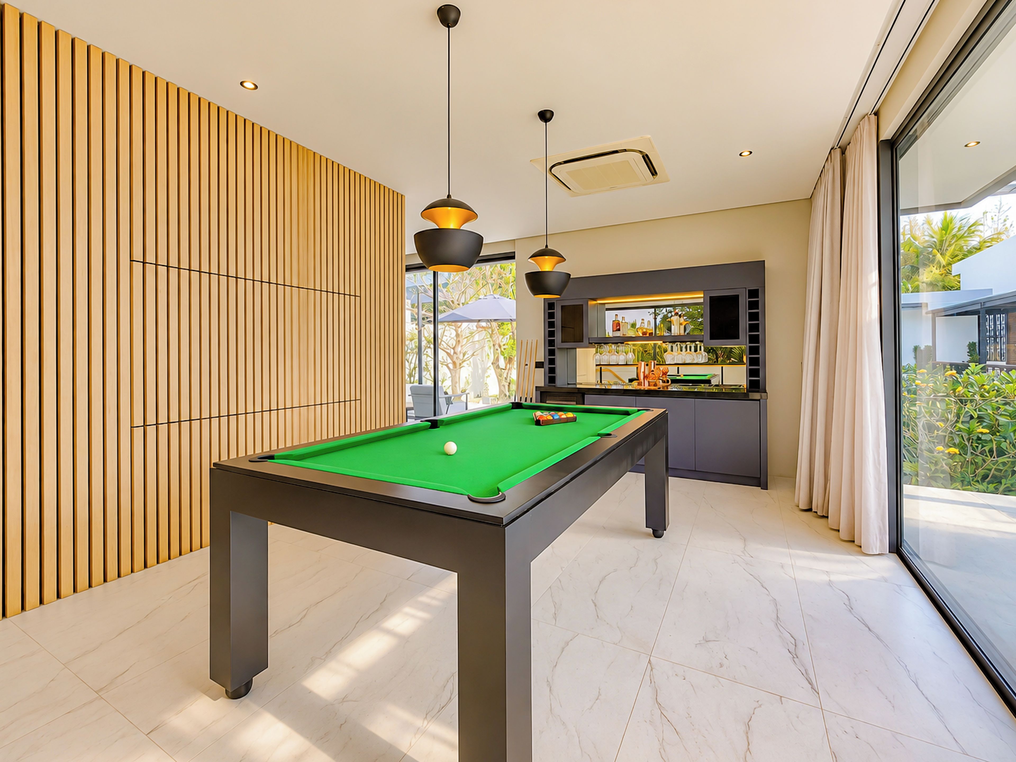 Una mesa de billar en una habitación moderna con pared de listones de madera, una zona de bar con botellas y vistas a través de un ventanal grande.