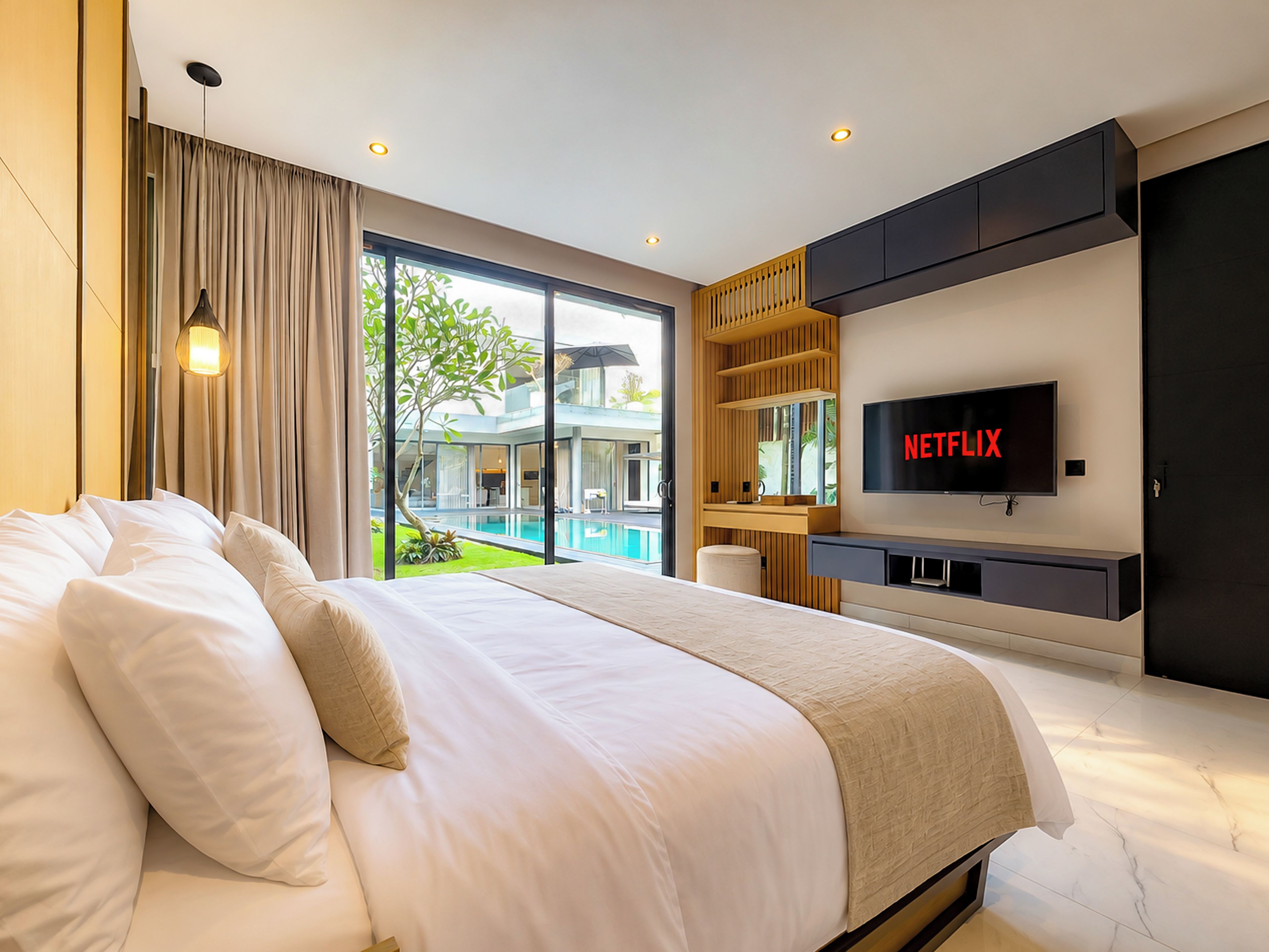 Ein modernes Hotelzimmer mit einem großen Bett, einem Fernseher, der 'NETFLIX' anzeigt, und Blick auf einen Swimmingpool durch die Glasdoor.