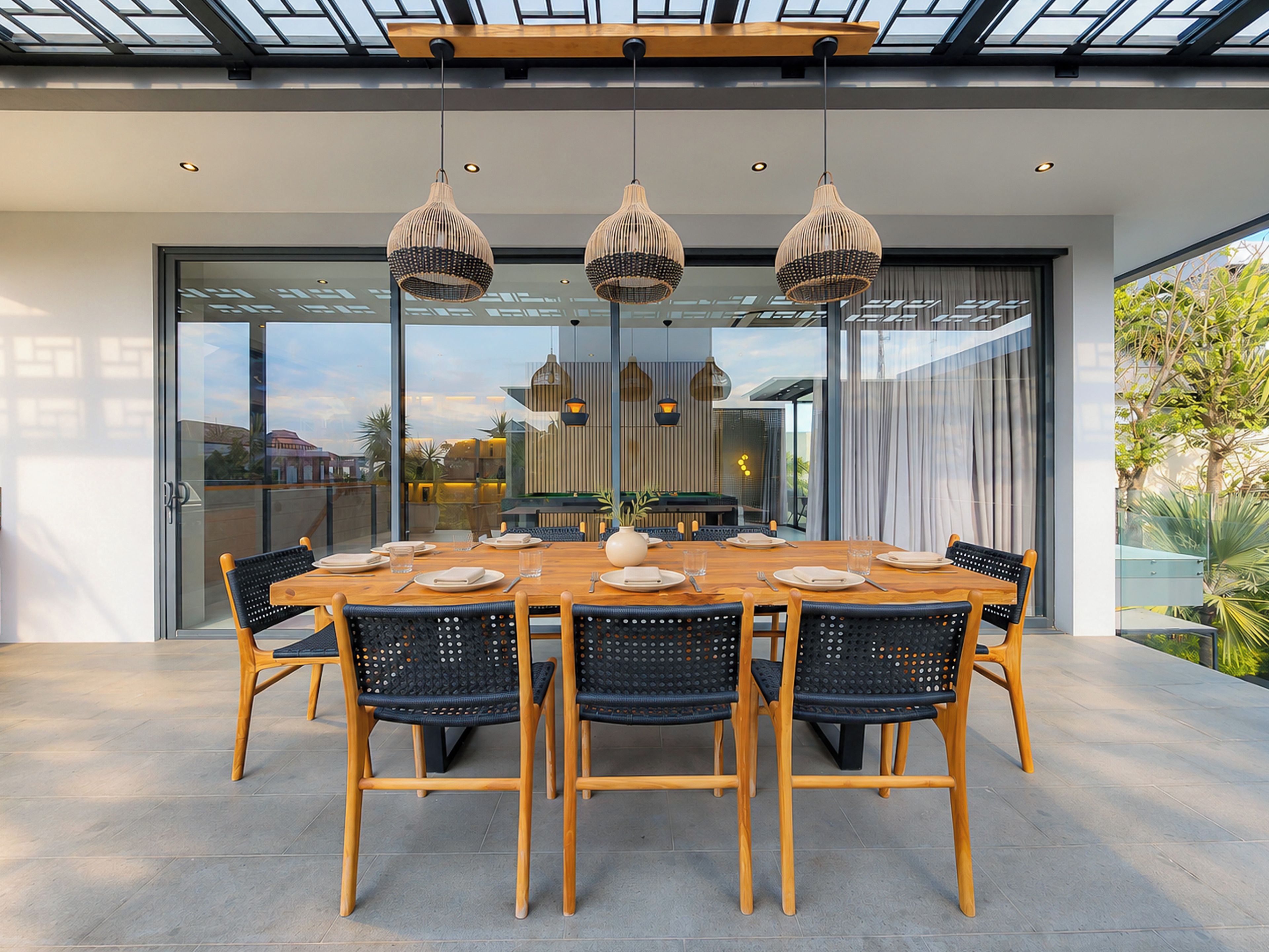 Un comedor moderno con una mesa cubierta por vidrio, sillas tejidas negras e iluminación colgante.