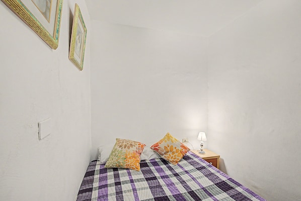 Une chambre à coucher avec une couvre-lit à carreaux, deux oreillers, une table de chevet avec une lampe et des tableaux encadrés accrochés au mur.