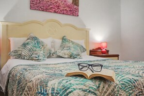 Una cama con una colcha estampada, almohadas y un libro abierto con gafas encima.