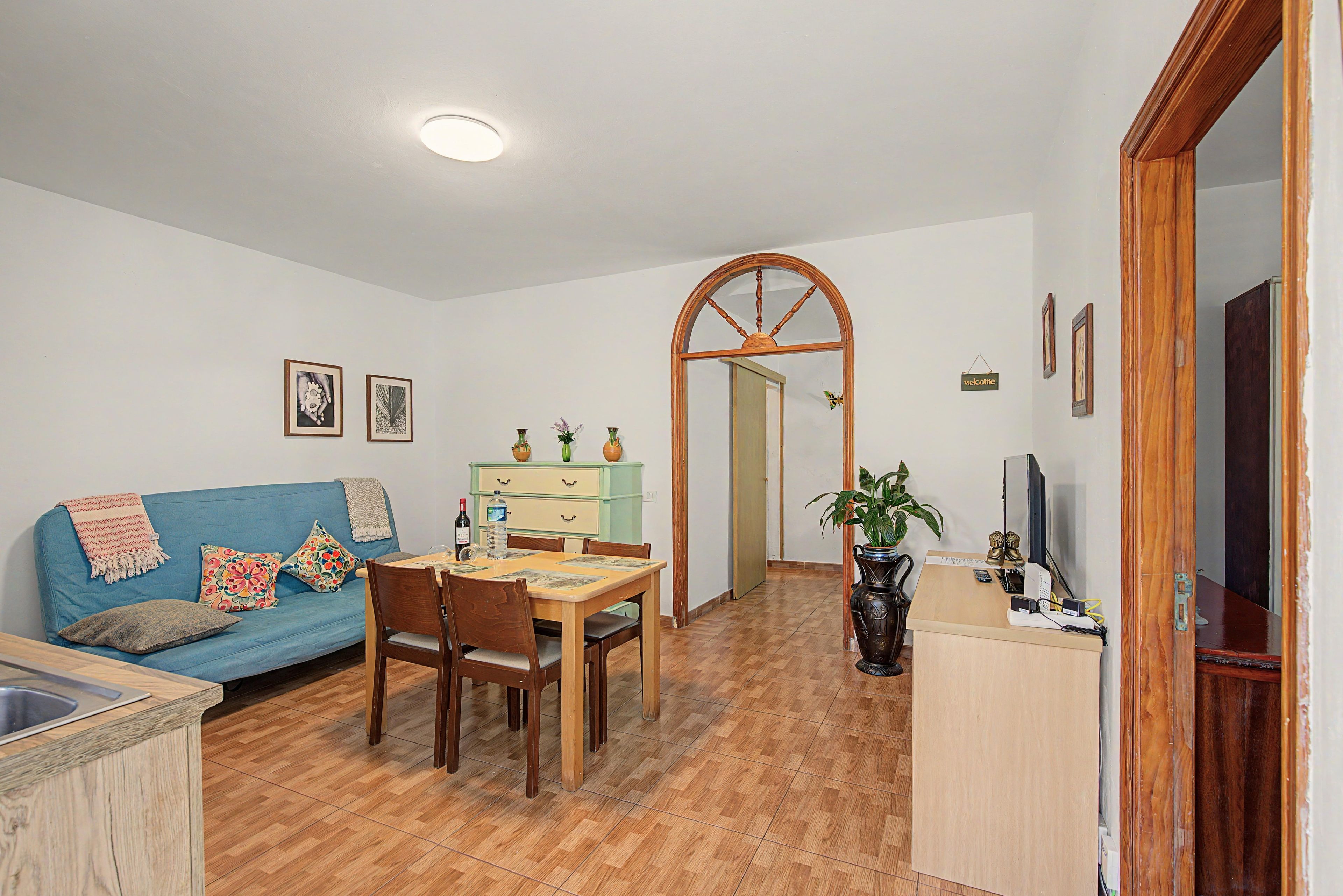 Una sala de estar con sofá, mesa de comedor, sillas, televisor y zona de cocina.