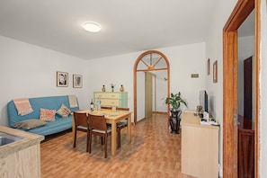 Un salon comprenant un canapé, une table à manger, des chaises, un téléviseur et un coin cuisine.