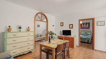 Una habitación con una mesa de comedor, sillas, un aparador de madera, un televisor y una cama con colcha estampada.