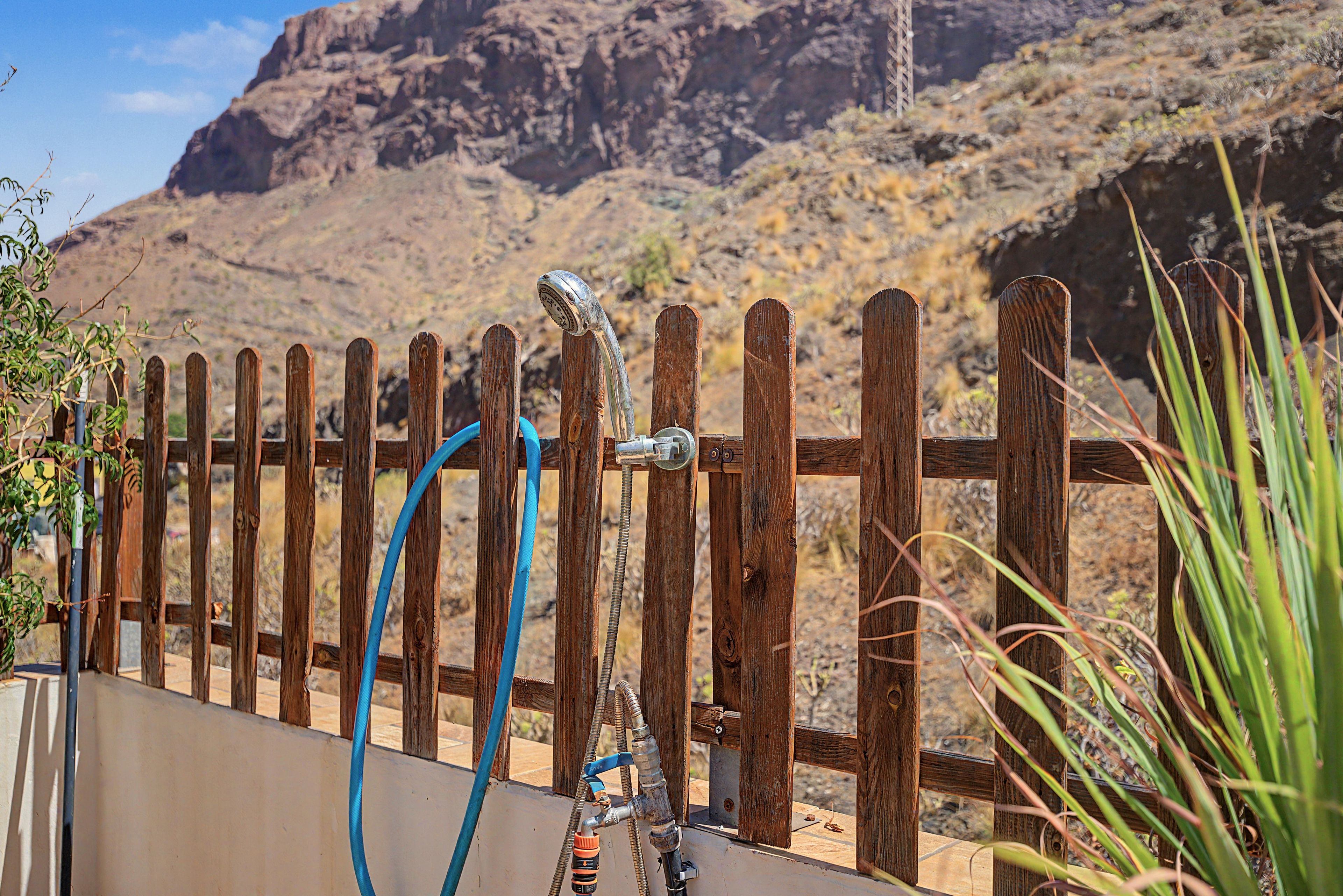 Una valla de madera con un grifo metálico y una manguera, con montañas al fondo.