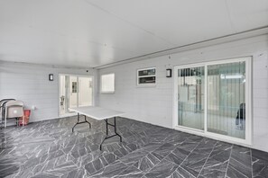 Una habitación amplia con una mesa y sillas blancas, un ventanal grande y una puerta que da a otra zona.