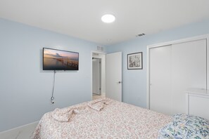 Un dormitorio con una cama, un televisor fijado a la pared y una puerta que da a otra habitación.
