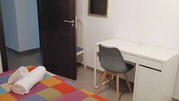 A room with a bed, a desk, a chair, and a door.