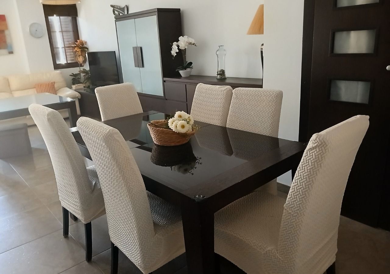 A dining area with a dark table, white upholstered chairs, and a centerpiece of flowers.