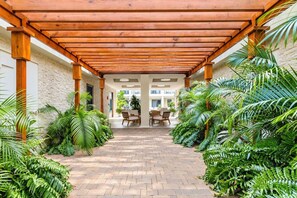 A covered walkway with a brick floor, surrounded by lush greenery and wooden pillars. - Wariruri 214 by Bocobay • Luxury Resort Stay (Noord)