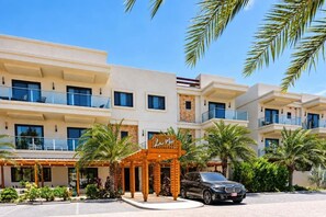 Un hotel de varios pisos con un diseño moderno, que cuenta con balcones, una entrada cubierta y un área de estacionamiento.